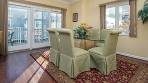 Comedor con mesa de vidrio, cuatro sillas, ventilador de techo y vistas a través de amplios ventanales correderas.