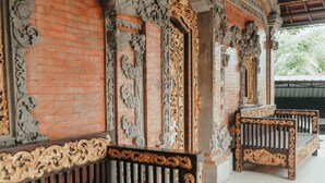 An ornate wooden bench with intricate carvings, a brick wall, and a metal railing. - Hotel Diana 2 (Denpasar)