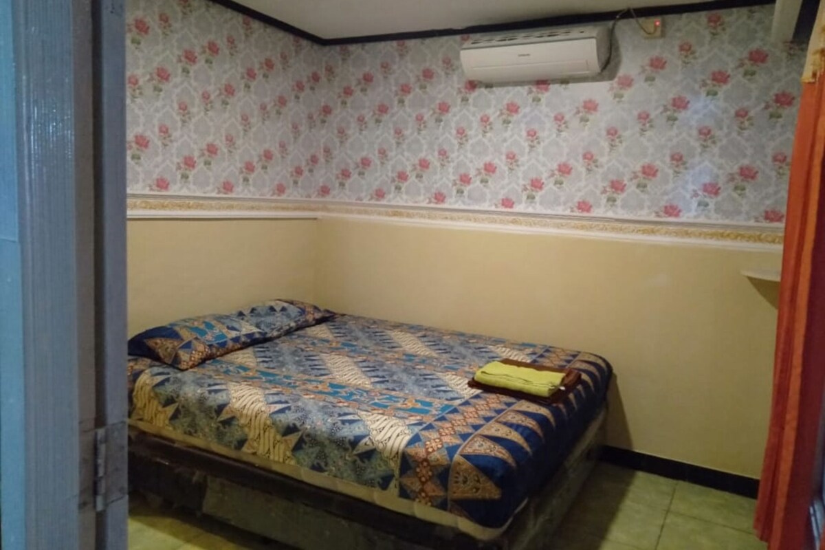 Ein kleiner Raum mit einem Bett, einer Wandklimaanlage und blumigem Wandpapier.