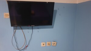 A television mounted on a wall with visible electrical wiring and three electrical outlets below it. - Lautze Residence (Jakarta)