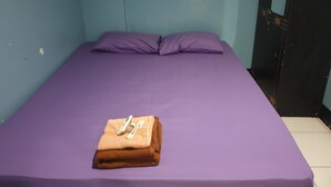 A single bed with a purple mattress and pillows, a folded brown blanket, and a pair of shoes on the bed. - Lautze Residence (Jakarta)