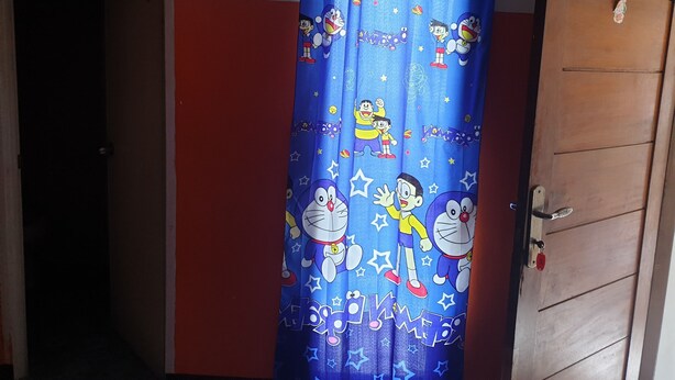 A room with a blue curtain featuring cartoon characters, a wooden door, and a red wall. - Lautze Residence (Jakarta)