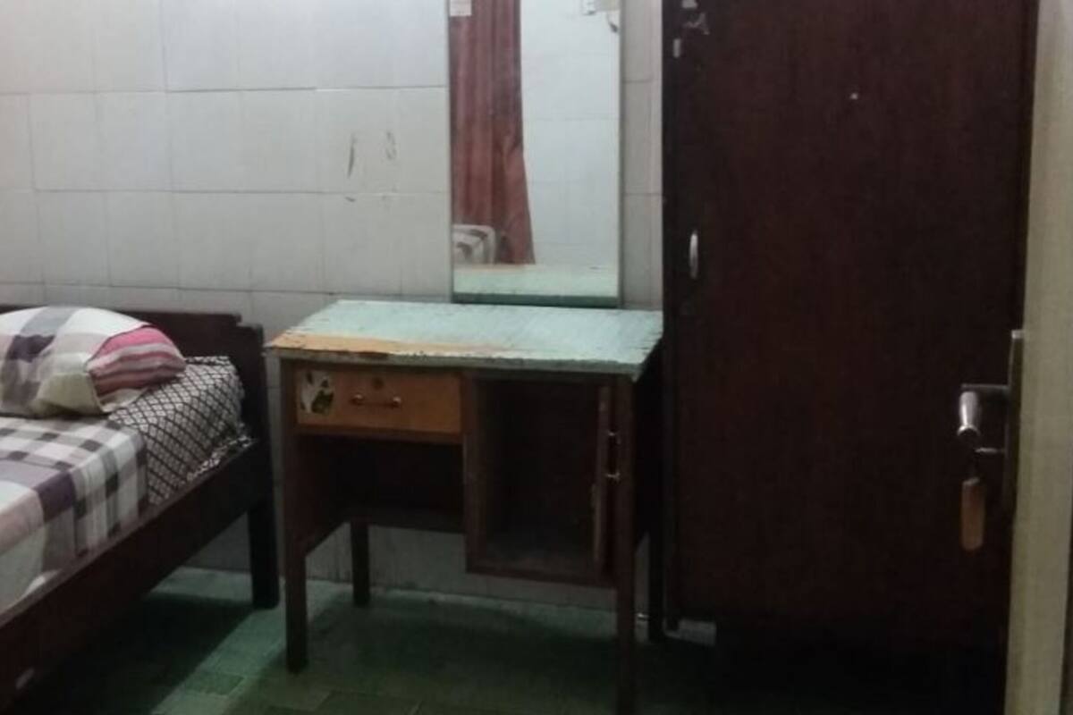 A small, dimly lit room with a single bed, a wooden desk, and a mirror.