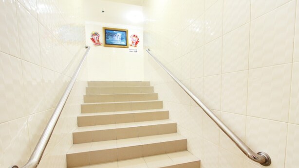 Un conjunto de escalones de cerámica color beige con barandales de metal, que conducen a una plataforma con cuadros enmarcados y un letrero.