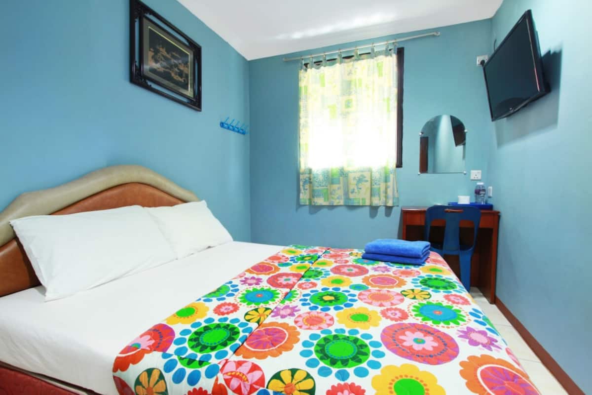 Un dormitorio con cama, escritorio, silla, televisor y ventana con cortinas.