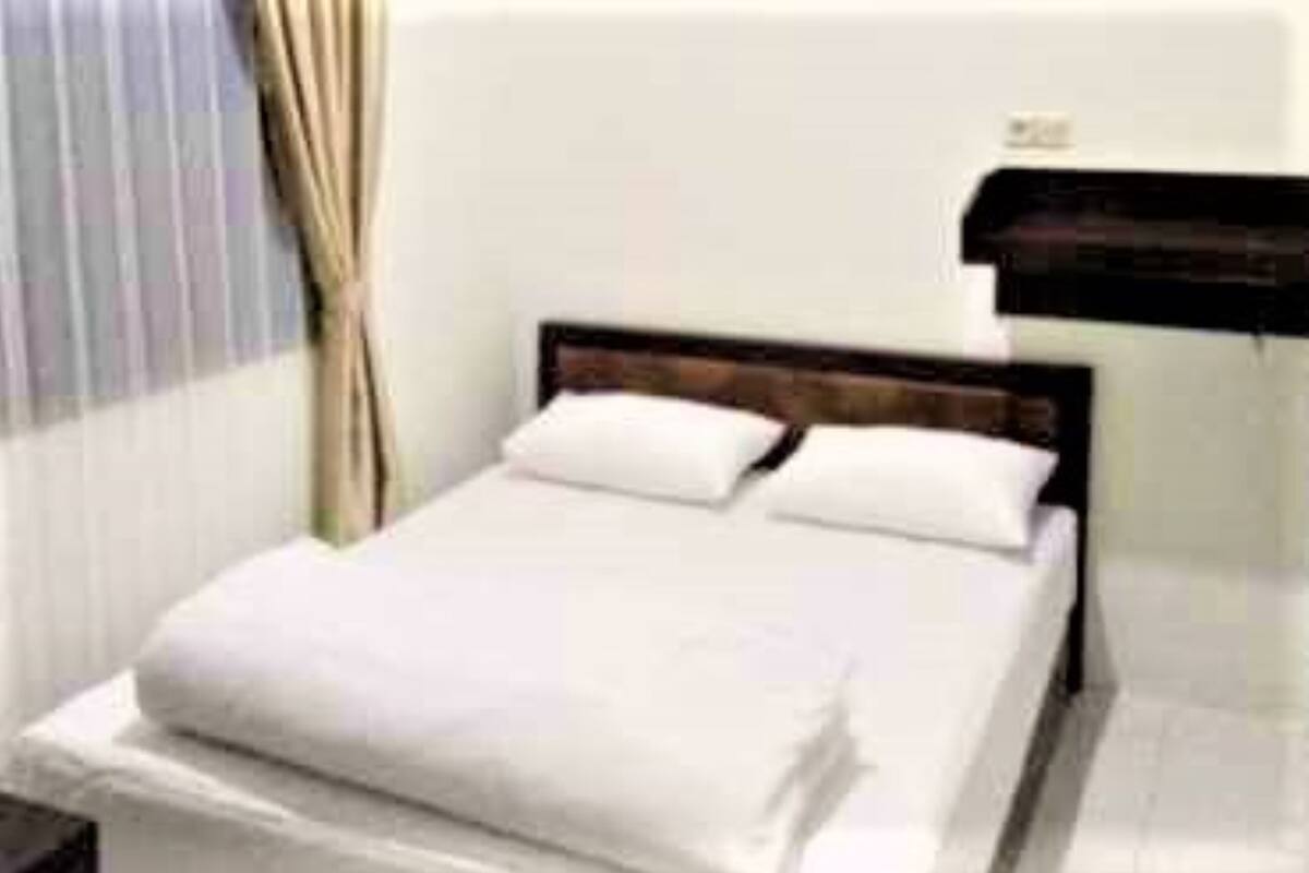 A neatly made bed with white linens in a room with a wooden headboard.