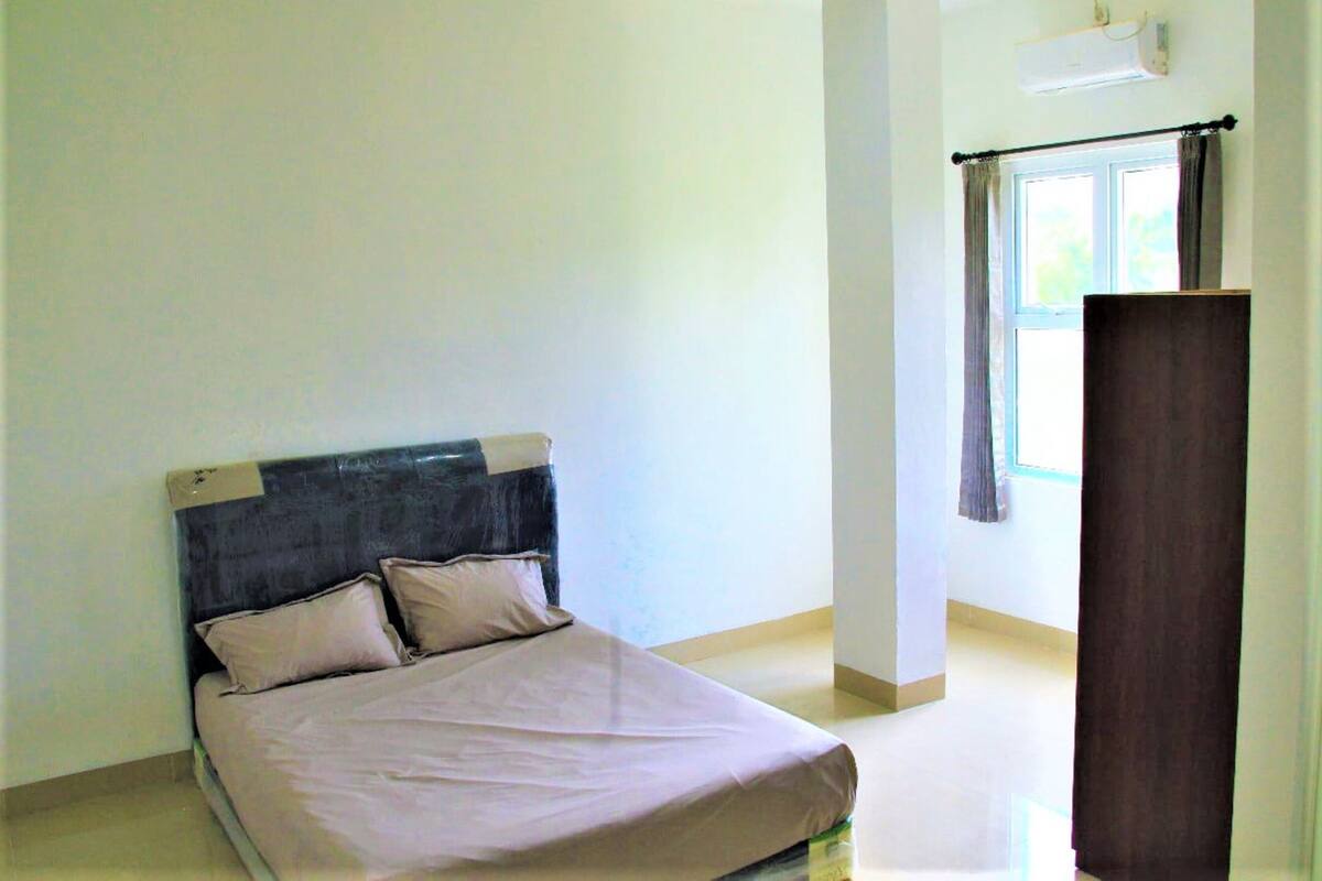 A bedroom with a bed, a window with curtains, and a wall-mounted air conditioner.