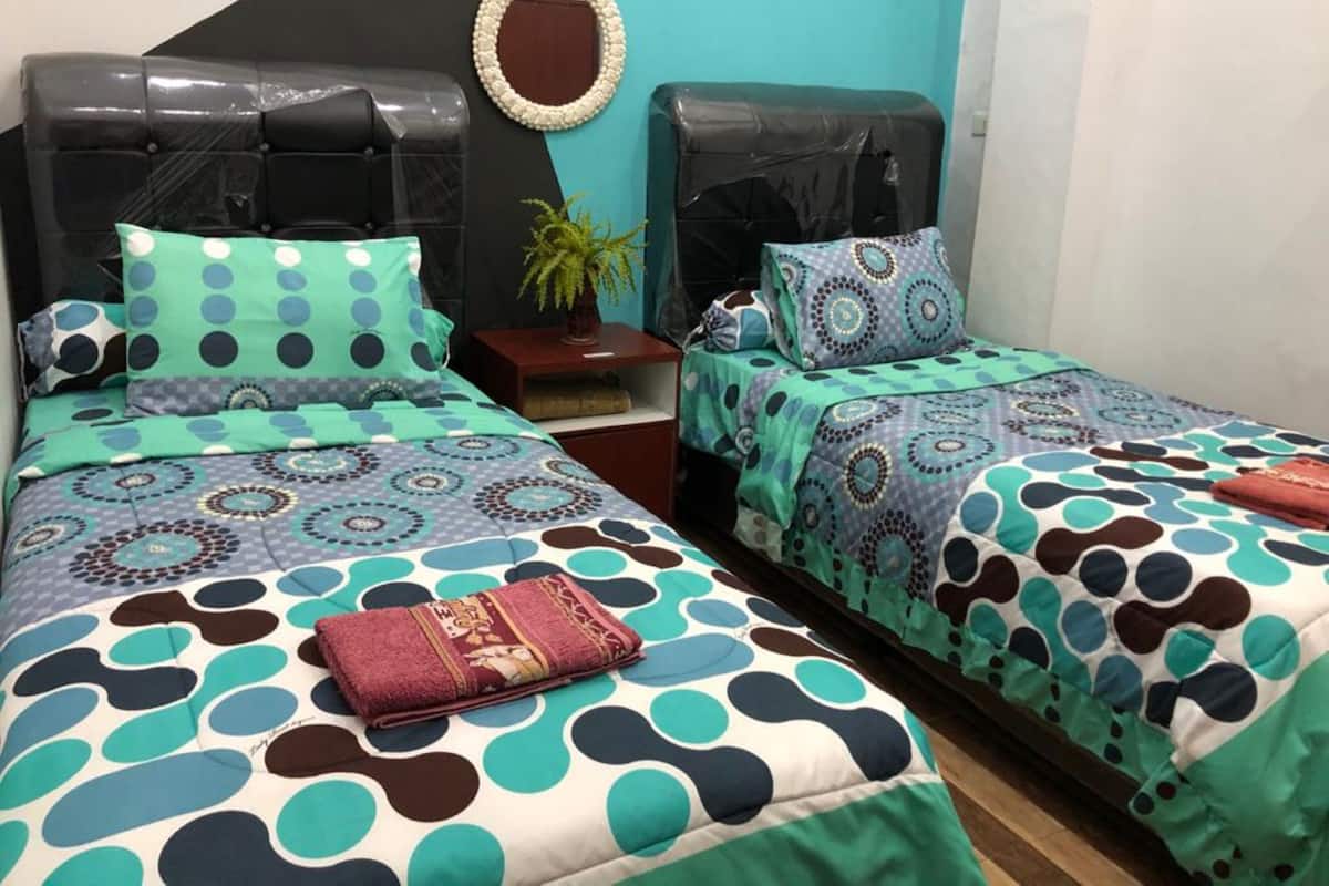 Ein Schlafzimmer mit zwei Betten, jeweils mit gemusterten Bettdecken und Kopfteilen. Es gibt einen kleinen Tisch mit Pflanze und einen Spiegel an der Wand.