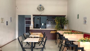 Una cafetería con varias mesas y sillas, una barra con una máquina de café y una planta decorativa.