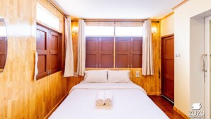 Ett hotellrum med träpanel på väggarna, en stor säng med vita sängkläder, två fönster med gardiner och en dörr på höger sida.