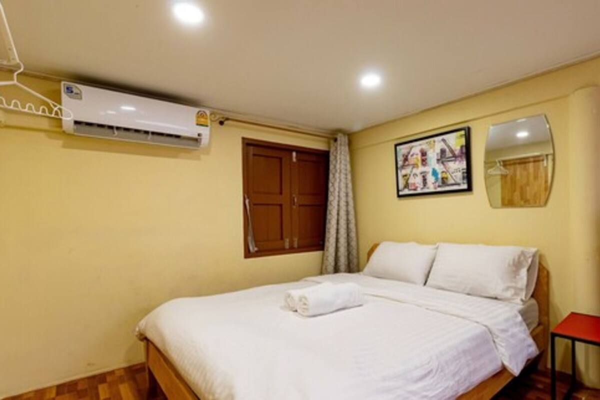A hotel room with a bed, a wooden door, an air conditioning unit, a framed picture on the wall, and a mirror.