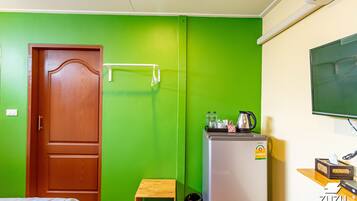 Habitación de hotel con pared verde, puerta de madera, taburete pequeño de madera, refrigerador y televisor montado en la pared.
