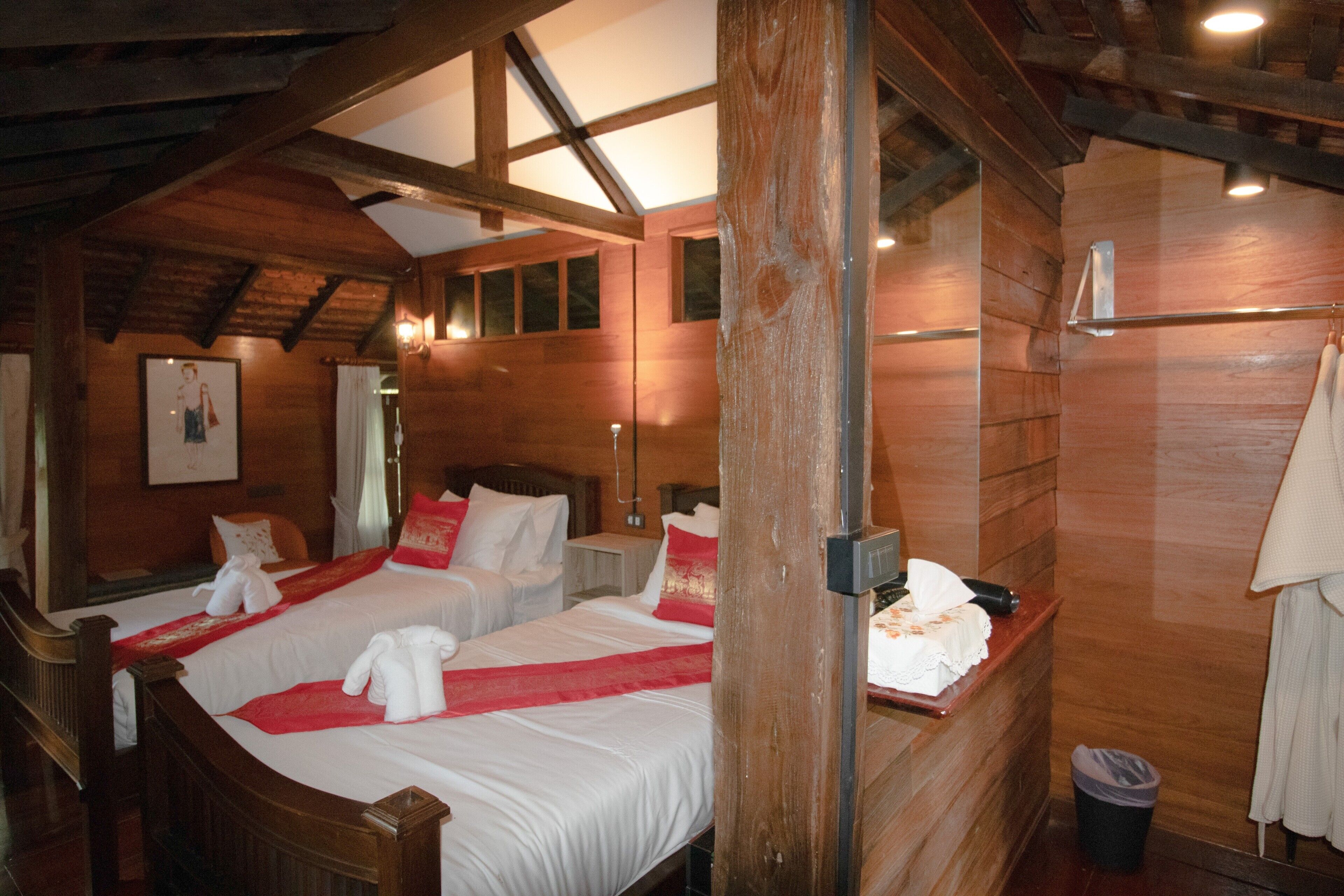 A wooden room with two beds, a wooden ceiling, and a window.