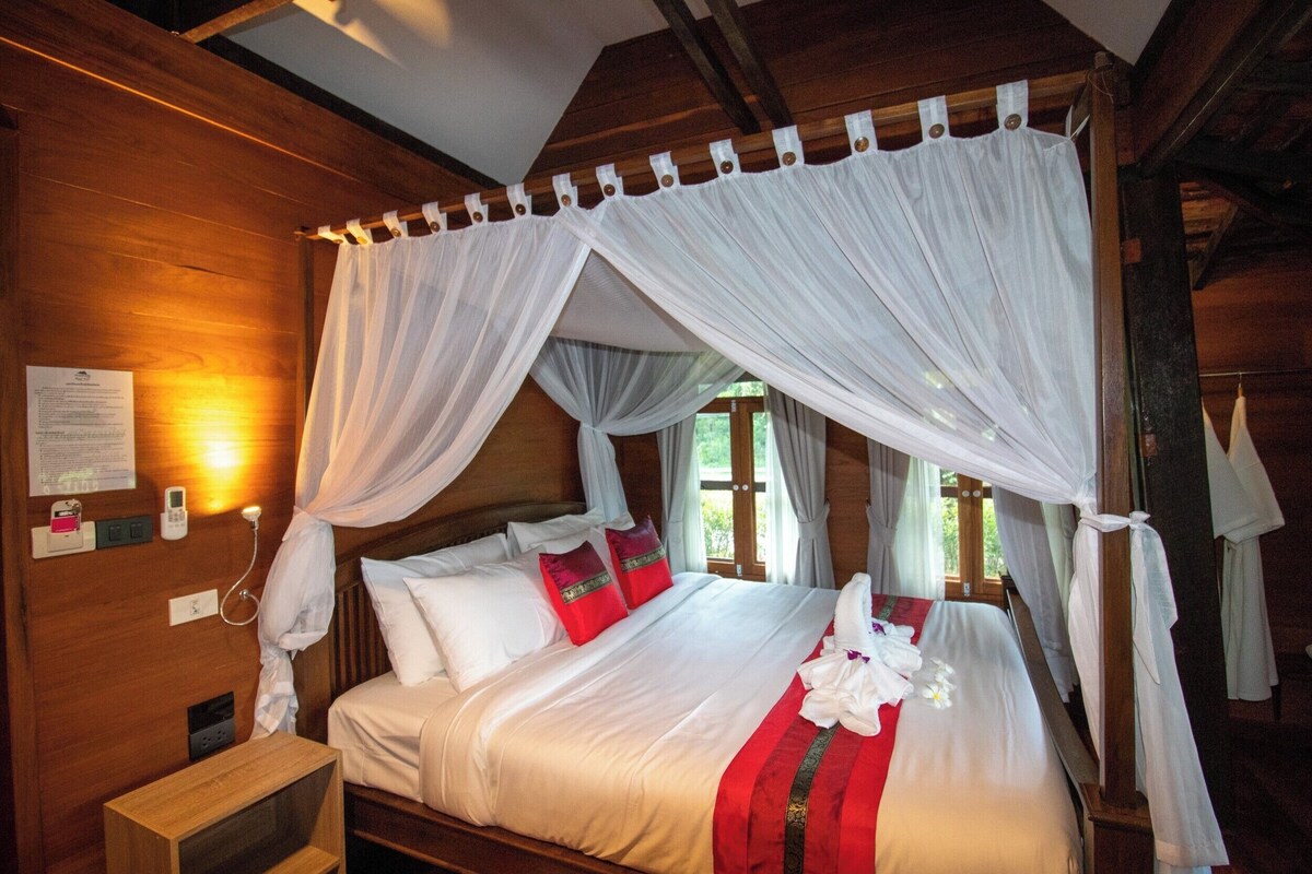 Een kamer met houten vloeren, een bed, witte gordijnen en een rood-wit dekbed.