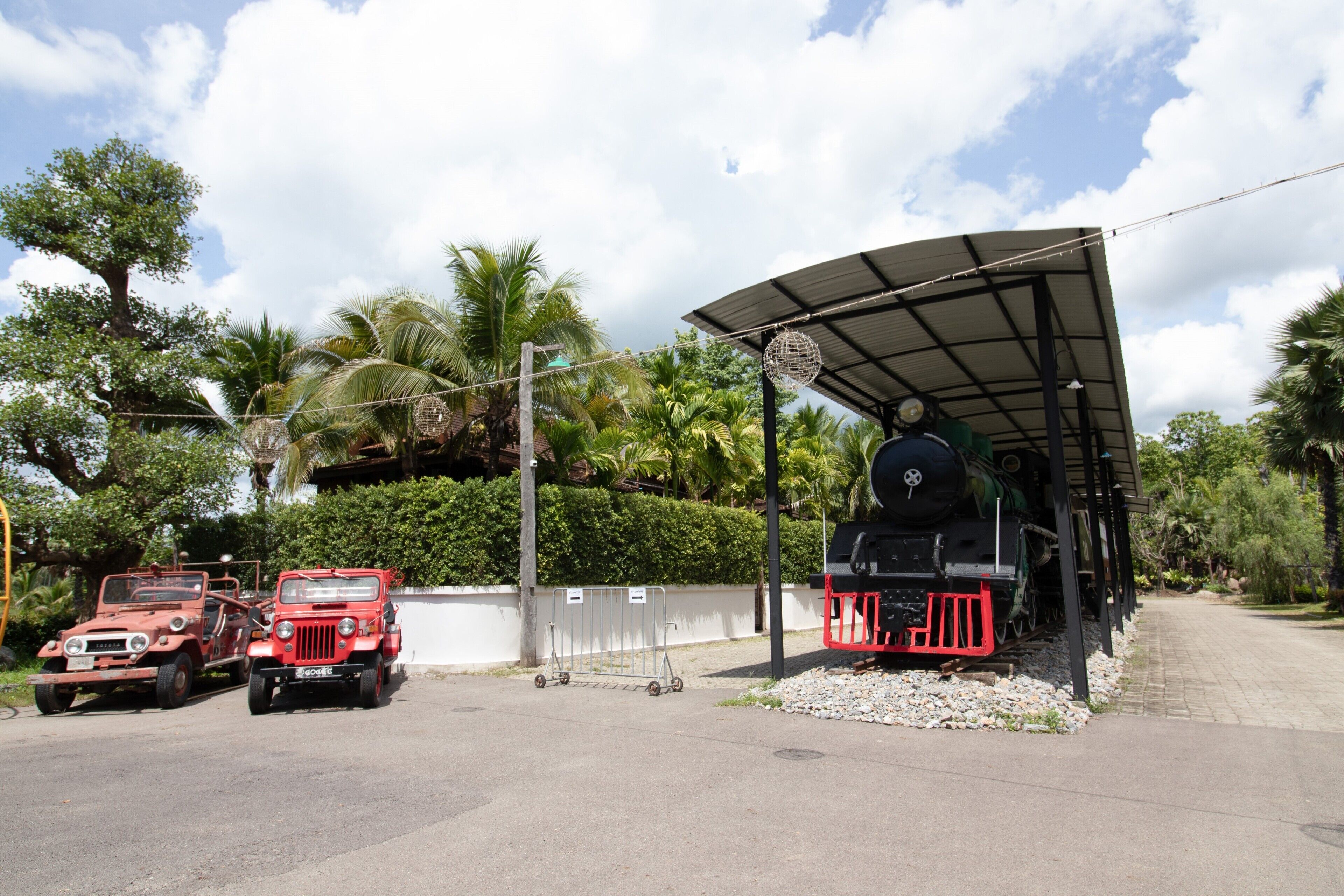 A train station with a covered waiting area, a vintage train, and two red vehicles.