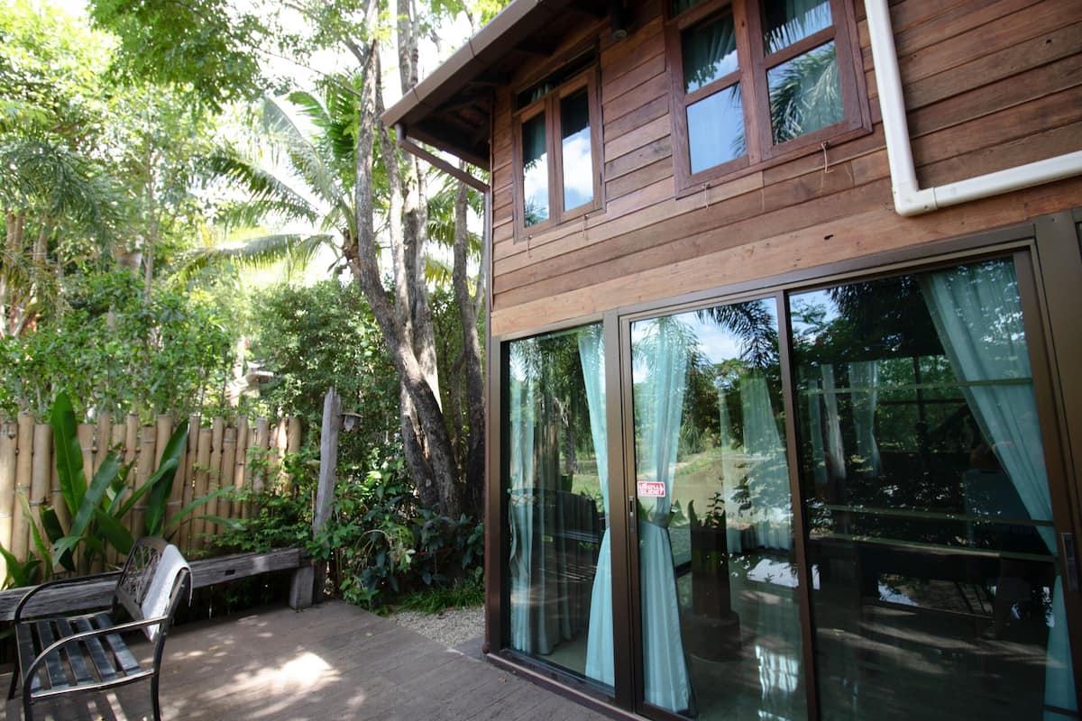 Een houten huis met grote glazen deuren en ramen, omgeven door weelderige begroeiing.