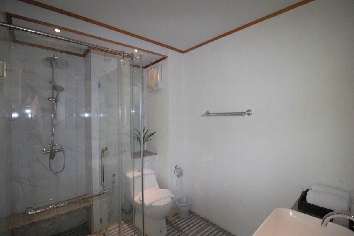 Un baño con ducha de vidrio, inodoro, lavamanos y toallero.