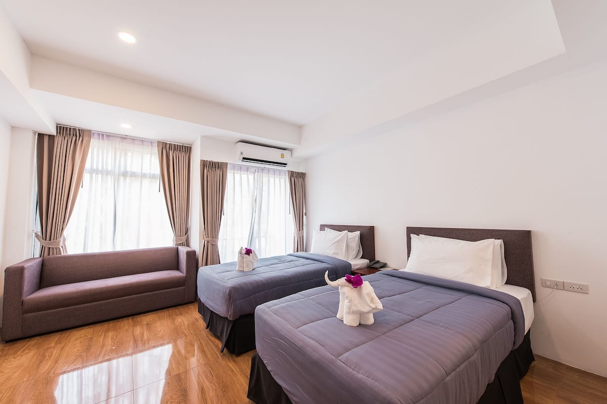 Een hotelkamer met twee bedden, een slaapbank en een airconditioner.