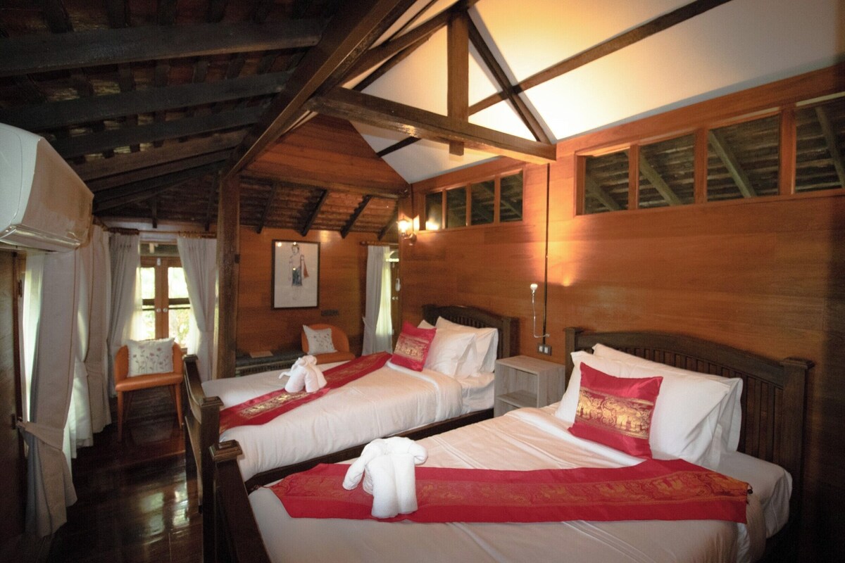 Een hotelkamer met twee bedden, houten wanden, een schuine plafond en een raam met gordijnen.