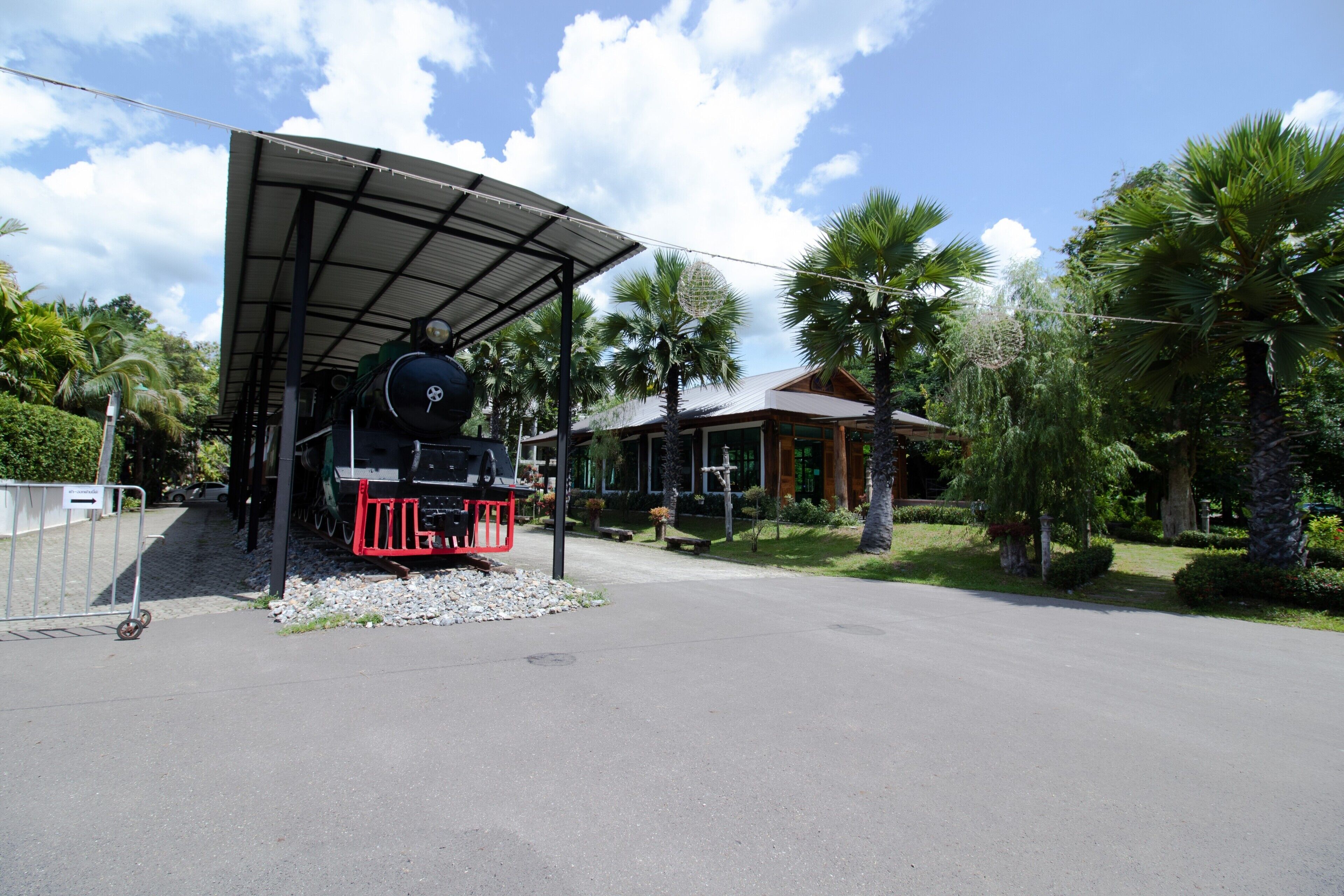 A covered outdoor area with a train, palm trees, and a building with a sloped roof.