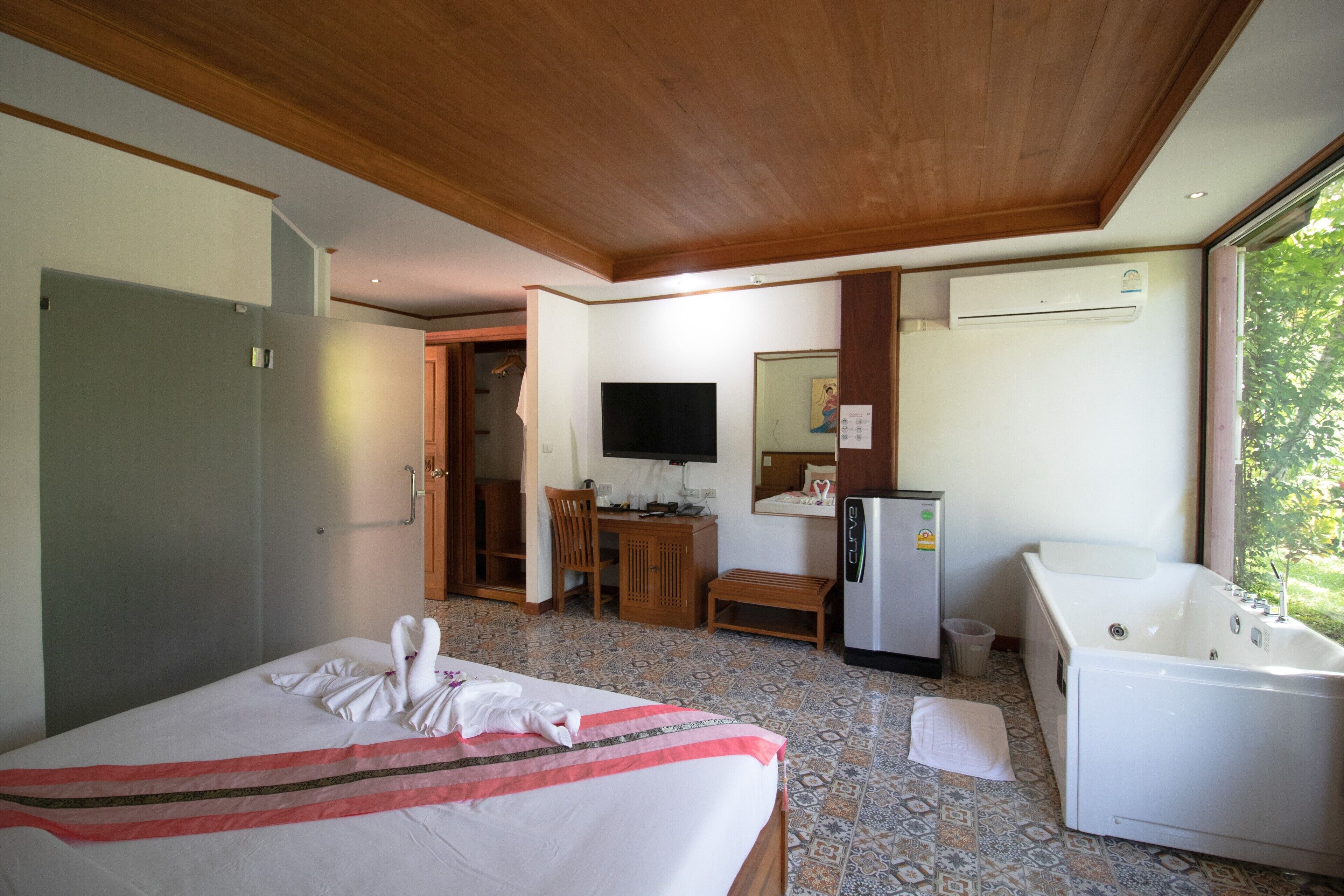 A hotel room with a bed, a desk, a TV, a mirror, a sink, and a bathtub.