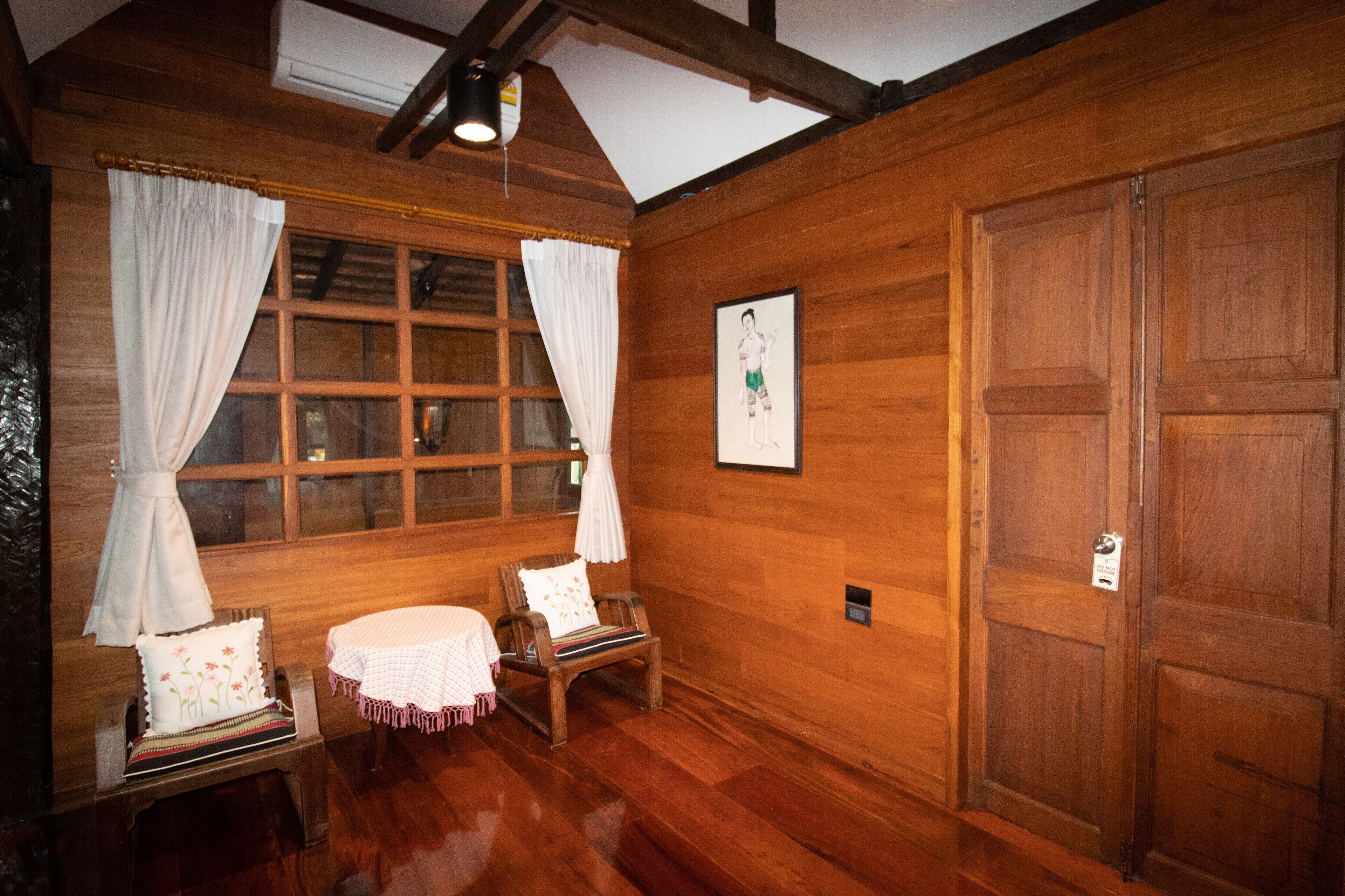 A wooden room with a large window, two chairs, a small table, and a wooden door.