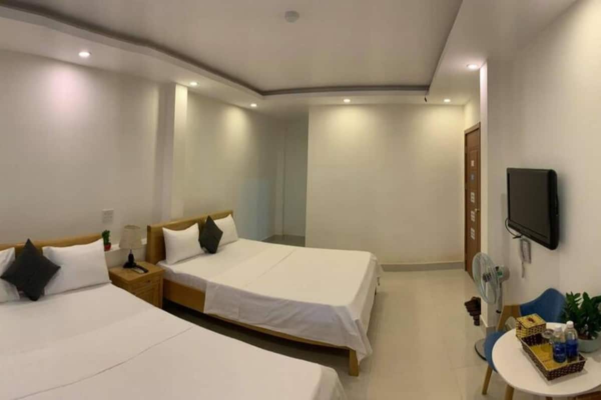 Une chambre d’hôtel avec deux lits, une télévision, une petite table avec un ventilateur et une porte.