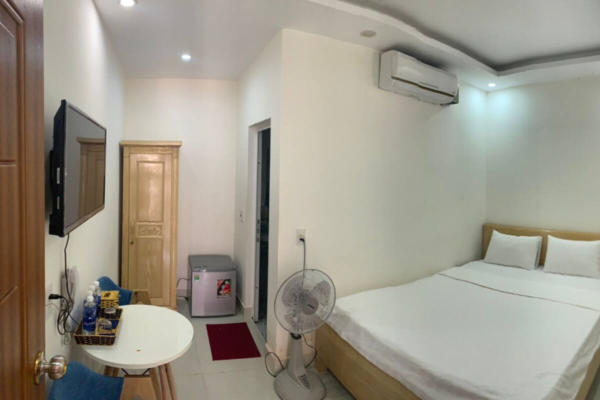 Une chambre d’hôtel comprenant un lit, un bureau avec une chaise, un petit réfrigérateur, un ventilateur et un appareil de climatisation.