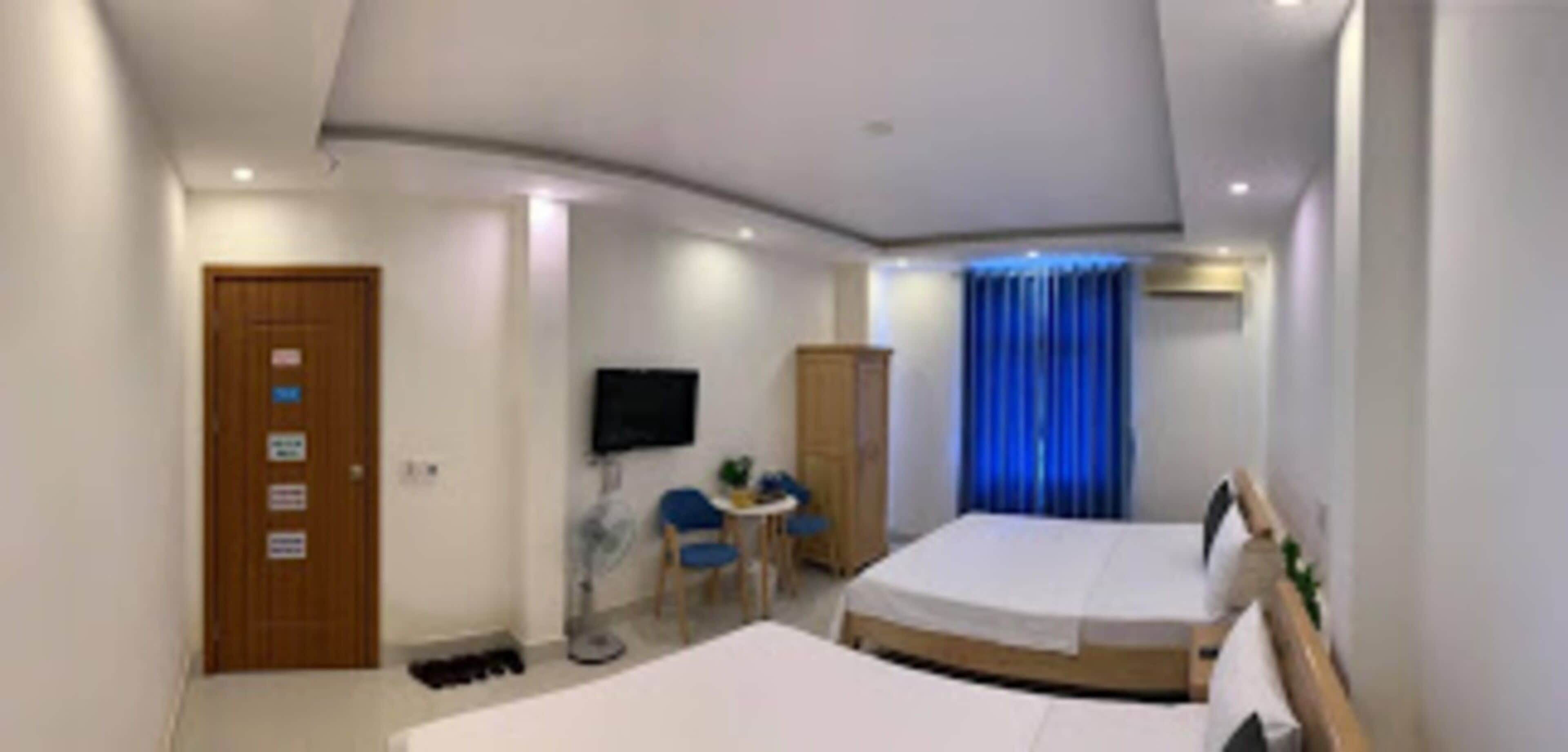 Ett hotellrum med två sängar, en tv, ett skrivbord med en stol, en garderob och en blå gardin.