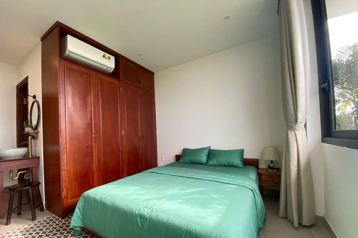 Een slaapkamer met een bed, een kledingkast, een bureau met een wastafel en een raam met gordijnen.