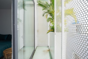 Une petite pièce aux murs de verre, avec un lit vert, un panier en osier et une plante.