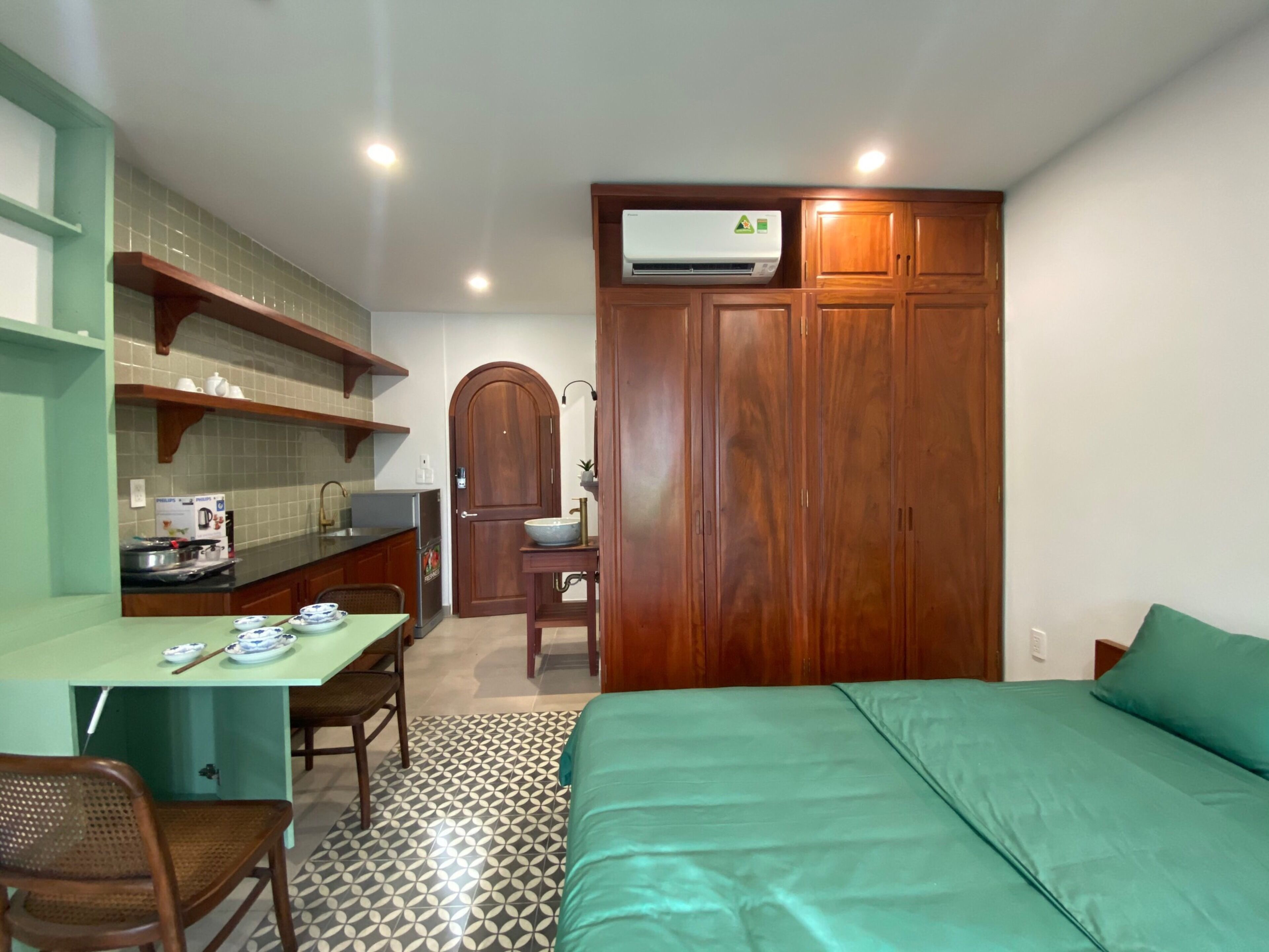 A compact room with a bed, a desk with a chair, a wardrobe, and a sink.