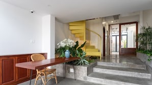 A modern interior with a wooden desk, a wicker chair, a blue vase with flowers, a concrete staircase, and a yellow spiral staircase.