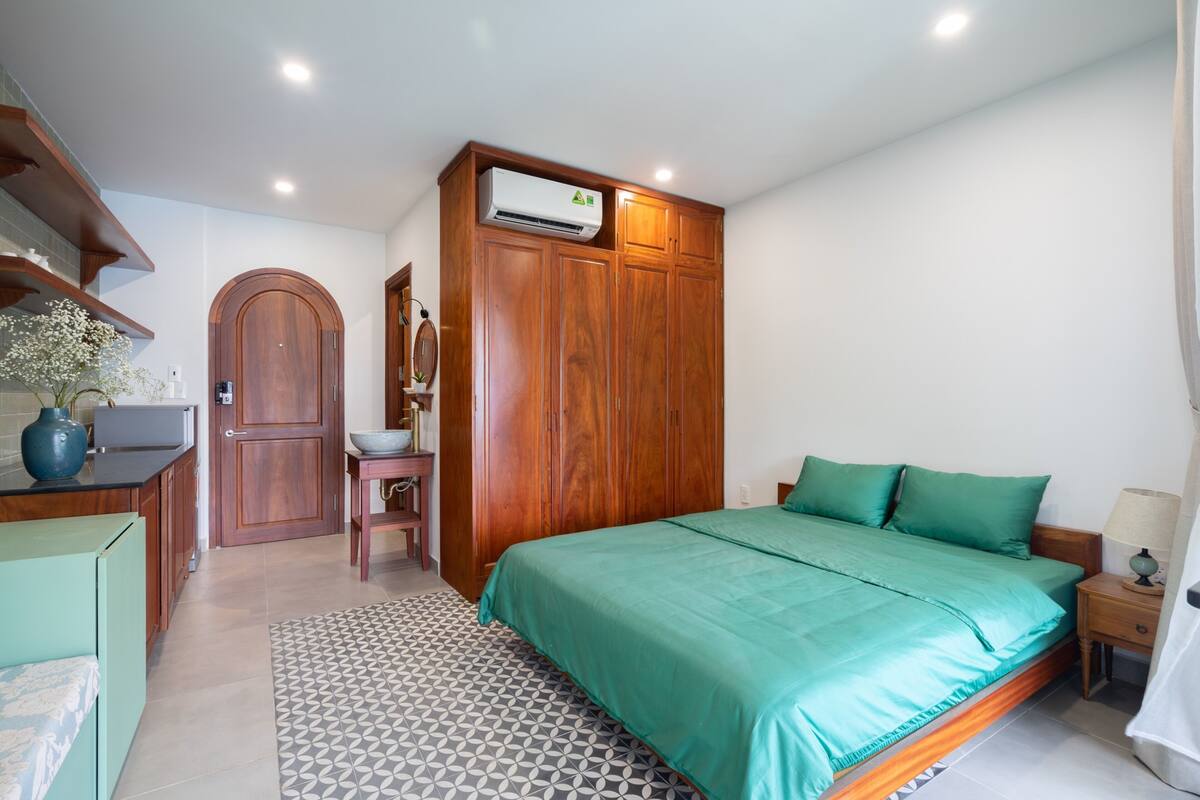 Een slaapkamer met een bed, een houten kledingkast, een ingebouwde airconditioning en een kleine tafel met een lamp.