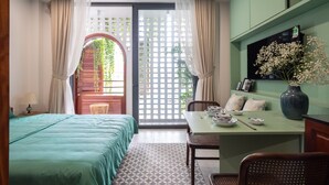 A room with a bed, a dining table with chairs, a vase with flowers, and a green wall with a shelf.