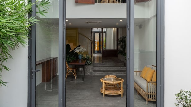 A modern house with a glass entrance leading to a dining area with a round table and wicker chairs.