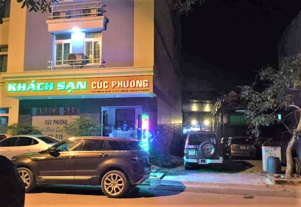 A building with a sign reading "KHÁCH SAN CỦC PHƯƠNG" and a parked SUV with emergency lights on.