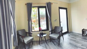 Ein Zimmer mit zwei Stühlen, einem kleinen Tisch, einem Kleiderschrank und einem Fenster mit Vorhängen.
