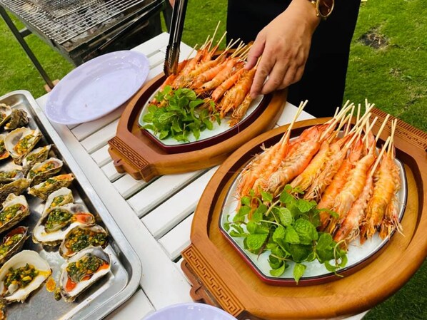 A table with plates of shrimp and oysters, a grill, and a person serving food.