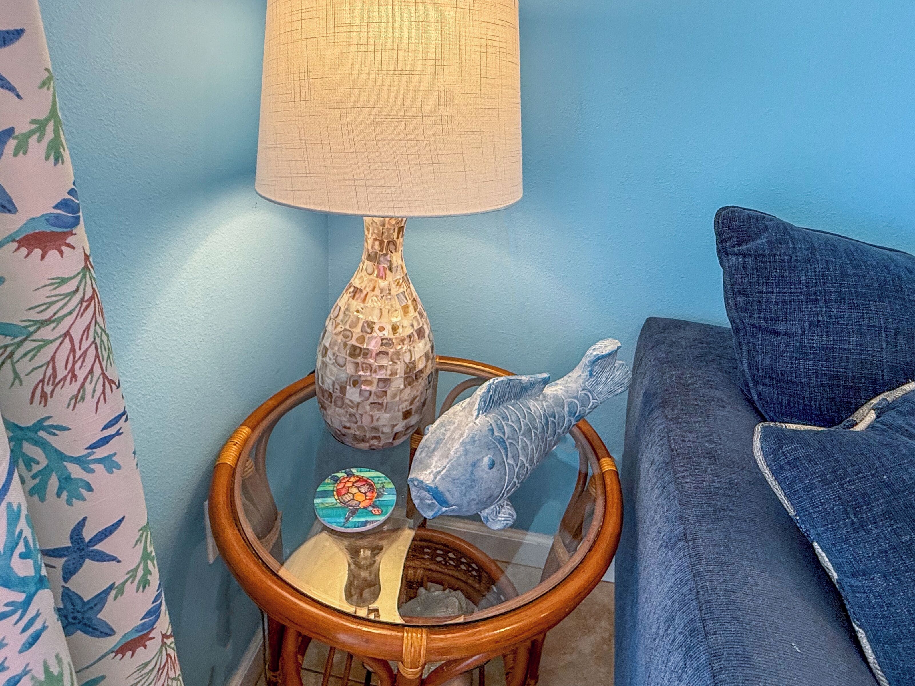 Una habitación con pared azul, una mesita de noche de madera con una lámpara, una escultura decorativa de un pez y un sofá azul.