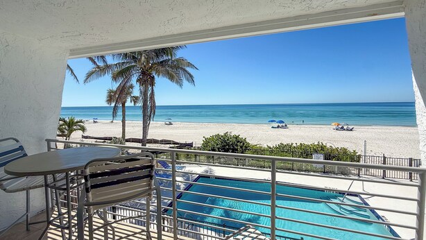 Un balcone con piscina che si affaccia su una spiaggia con palme e ombrelloni.