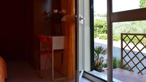 Une pièce comprenant un bureau, une chaise, un téléviseur fixé au mur et donnant sur un jardin par la porte.