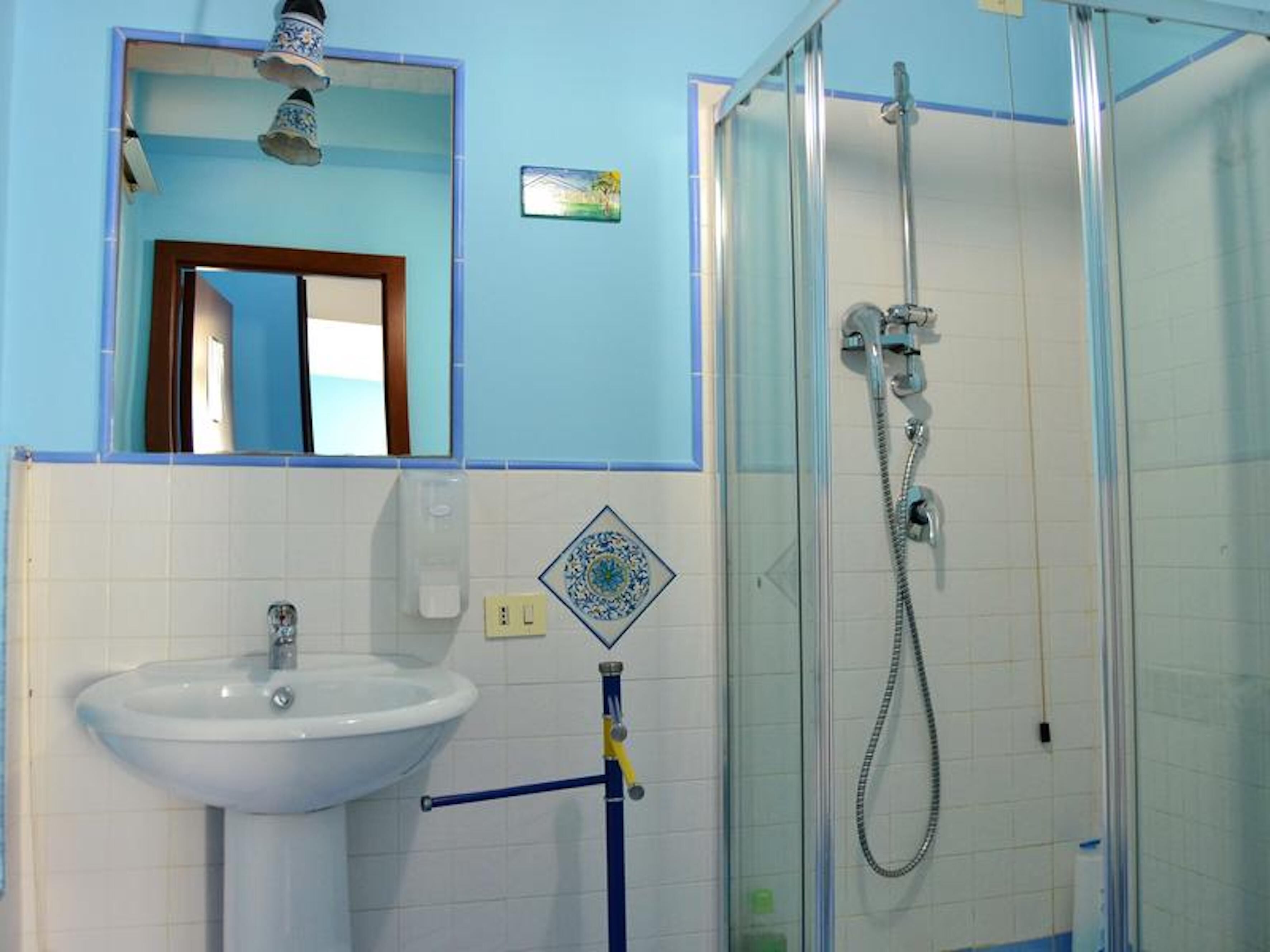 Baño con lavamanos blanco, espejo, cabina de ducha y toallero azul.