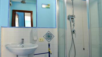 Baño con lavamanos blanco, espejo, cabina de ducha y toallero azul.