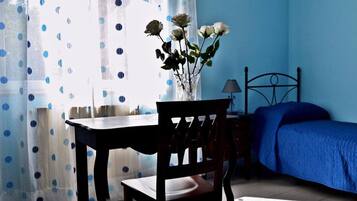 Un dormitorio con cama, mesita de noche, una silla, lámpara y ventana con cortinas.