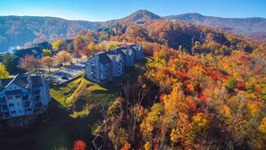 A multi-story building with a flat roof, surrounded by a lush, colorful autumn forest. - Vibrant Vacay - Studio Loft for 4 with Deck, Wifi, Hot Tub & Pools (Gatlinburg)