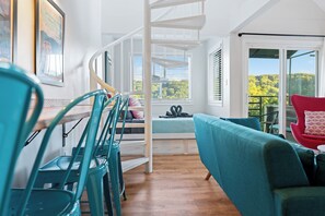 A room with a spiral staircase, a sofa, a dining table with chairs, and a view of greenery outside.