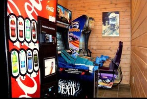 A room with a gaming arcade, a Coca-Cola vending machine, and a poster on the wall. - Vibrant Vacay - Studio Loft for 4 with Deck, Wifi, Hot Tub & Pools (Gatlinburg)