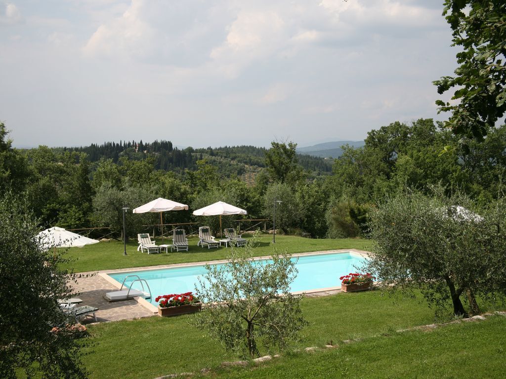 A swimming pool with lounge chairs and umbrellas, surrounded by greenery and hills in the background.