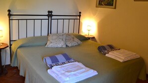 Ein ordentlich bezogenes Bett mit Metallkopfteil, zwei Kissen und einer gefalteten Decke. Auf beiden Seiten des Bettes stehen jeweils eine Nachttischlampe.